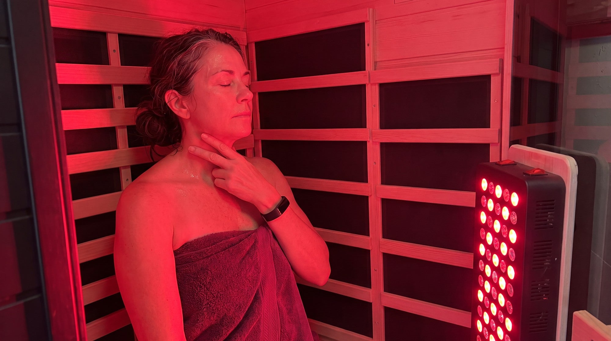 Woman in her 50s in a SaunaBox Solara, bathed in red light from the panel