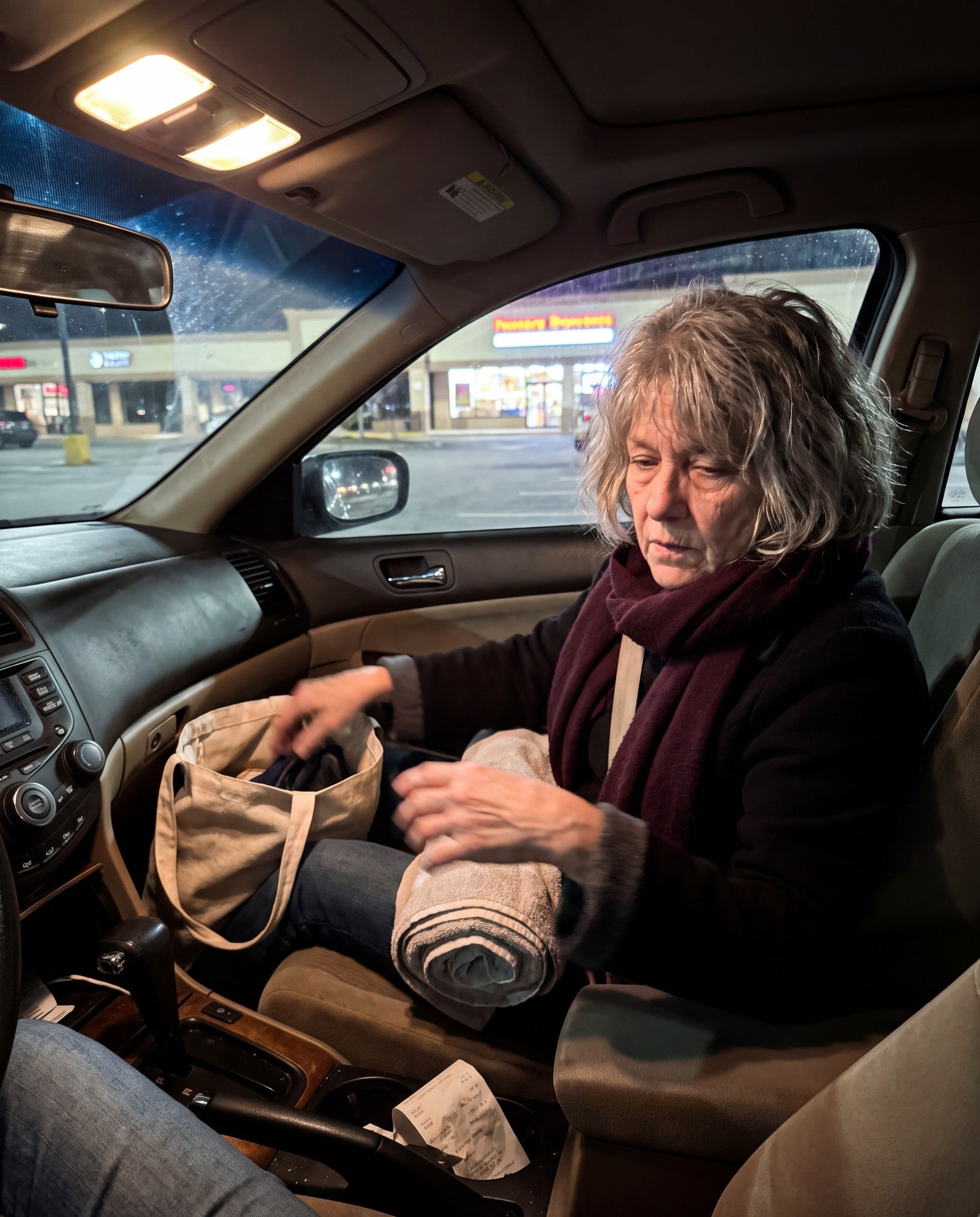 Woman in her 50s in her car at night, packing a towel and tote bag after the spa