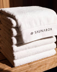 SaunaBox 100% cotton full body towels, stack of five folded on a cedar sauna bench