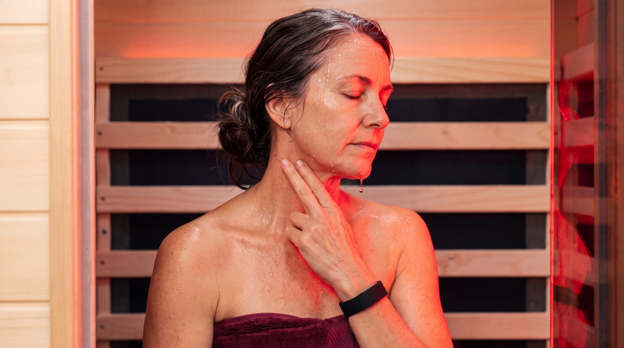 Woman in her 50s in a SaunaBox Solara, bathed in red light from the panel
