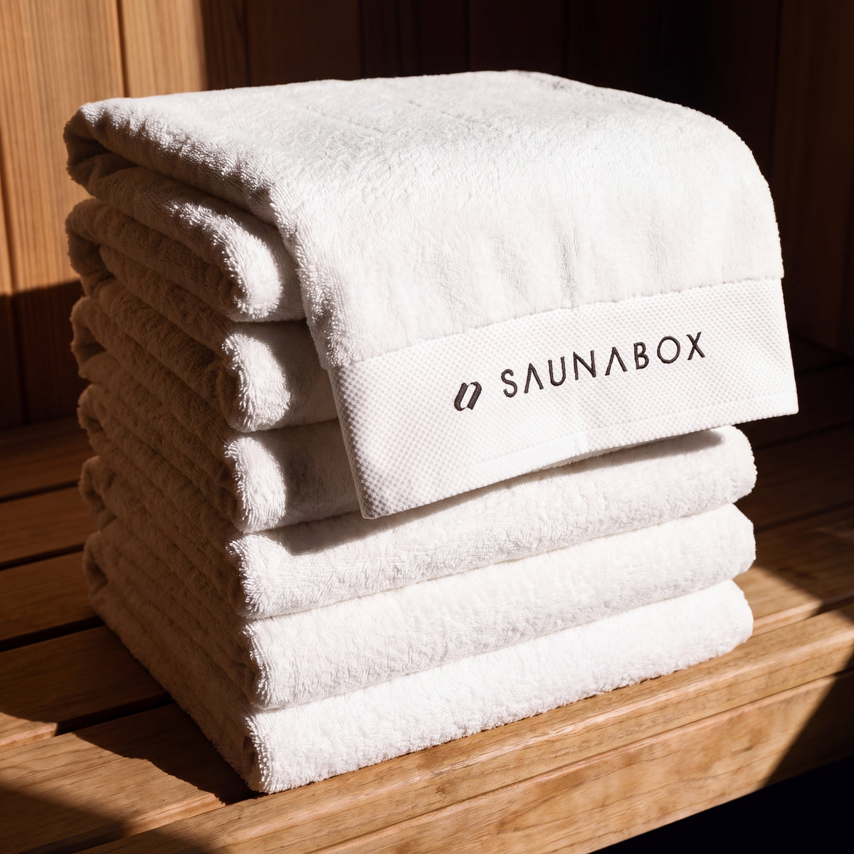SaunaBox 100% cotton full body towels, stack of five folded on a cedar sauna bench